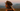 A side-profile portrait of a young woman wearing a brown cap outdoors at dusk, with a soft blurred landscape in the background and orange-red text overlay reading “TV Grain Film Specks & Dirt - Light” near the bottom.